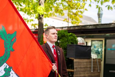 Klagenfurt, Austria - October 04, 2025: Young man dressed in traditional clothing holds a colorful flag at Erntedankfest, embodying festive atmosphere and cultural pride