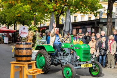 Klagenfurt, Austria - October 04, 2025: Man on green tractor waves at crowd during Erntedankfest in Benediktinermarkt, showcasing vibrant autumn festivities
