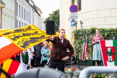 Klagenfurt, Austria - October 04, 2025: Man dressed in traditional clothing waves flag at Erntedankfest in Benediktinermarkt, highlighting festive atmosphere