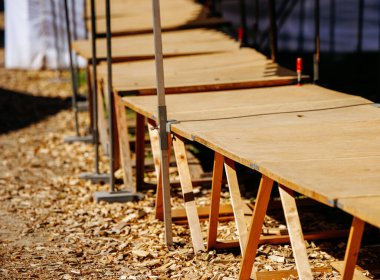 Wooden outdoor construction site with sawdust and temporary platforms on sunny day.