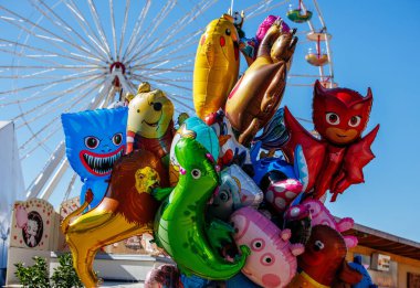 St Veit An Der Glan, Austria - October 03, 2025: Colorful balloons shaped like cartoon characters are displayed at St. Veiter Wiesenmarkt, with a ferris wheel behind