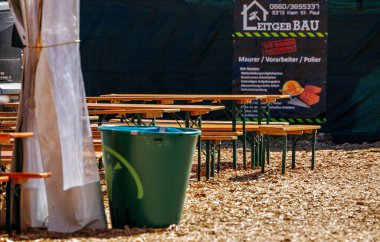 St Veit An Der Glan, Austria - October 03, 2025: Outdoor seating area at St. Veiter Wiesenmarkt features wooden benches and a green trash bin, creating a lively festival environment