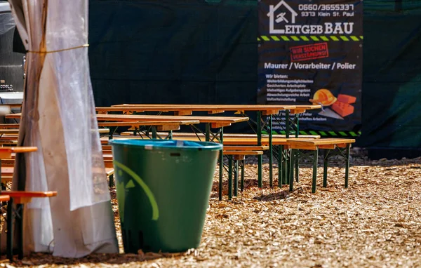 St Veit An Der Glan, Austria - October 03, 2025: Outdoor seating area at St. Veiter Wiesenmarkt features wooden benches and a green trash bin, creating a lively festival environment
