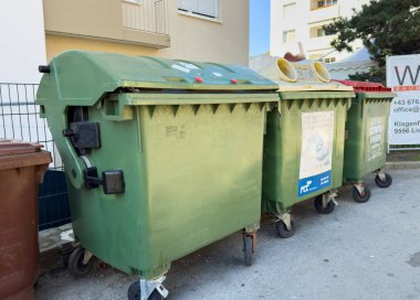Villach, Austria - October 09, 2025: Green waste containers positioned beside a building, highlighting recycling initiatives and urban cleanliness with copy space