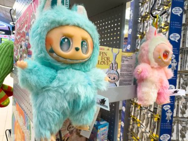 Villach, Austria - October 09, 2025: Colorful plush toys are hanging in a store, featuring a blue furry creature and a pink one with cute expressions and textures