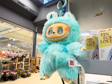 Villach, Austria - October 09, 2025: Turquoise plush toy with big eyes is displayed in a store, surrounded by vibrant flowers and various merchandise