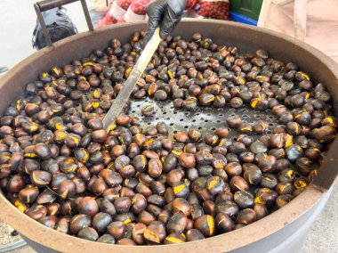 Freshly roasted chestnuts stirred in large pan at outdoor market.