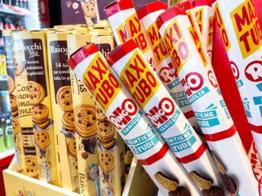 Trieste, İtalya - 14 Ekim 2025: Tatlı seçeneklerle dolu bir bakkal koridorunda çeşitli kurabiye paketlerinin yanında parlak renkli MAXI TUBO dondurma külahları