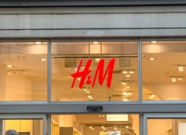 Trieste, İtalya - 14 Ekim 2025: H & M mağaza girişinde ikonik kırmızı logo ve parlak iç ışıklar yer alıyor ve karşılayıcı bir alışveriş ortamı yaratıyor