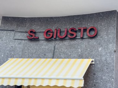 Trieste, İtalya - 14 Ekim 2025: S. Giusto Restoran tabelası sarı çizgili tente ile gri taş duvara kırmızı harfleri gösteriyor.