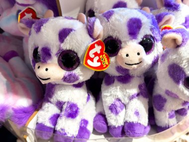 Trieste, İtalya - 14 Ekim 2025: Büyük gözlü şirin mor ve beyaz peluş inek oyuncağı, diğer doldurulmuş hayvanlarla çevrili renkli bir oyuncakçıda sergileniyor.