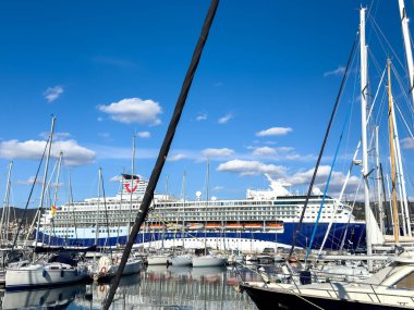 Trieste, İtalya - 14 Ekim 2025: Büyük yolcu gemisi açık gökyüzü ile canlı bir deniz manzarası yaratarak yelkenli ve yatlarla marinada demirlemiştir.