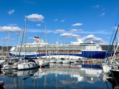 Trieste, İtalya - 14 Ekim 2025: Büyük yolcu gemisi açık mavi gökyüzü altında sakin sularda yansımalar yaratarak yelkenlilerle marinada demirlemiştir.