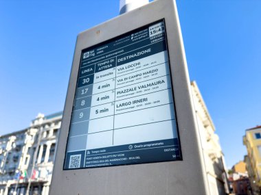 Trieste, İtalya - 14 Ekim 2025: Toplu taşıma bilgi panosu, tarihi binaların bulunduğu canlı bir şehir atmosferinde otobüs varış saatlerini ve varış noktalarını gösteriyor