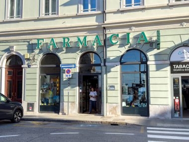 Trieste, İtalya - 14 Ekim 2025: Farmacia girişi şehir dükkanları ve sokak unsurlarıyla çevrili yeşil harfler ve davetkar bir atmosfer içeriyor