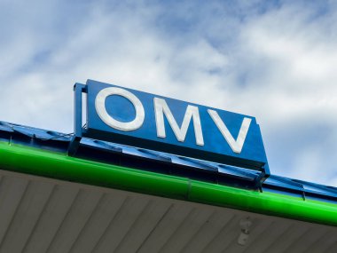 Althofen, Avusturya - 17 Eylül 2025: OMV benzin istasyonu işareti bulutlu bir gökyüzünün altında, markanın kimlik ve hizmet tekliflerini vurguluyor