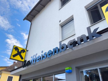 Althofen, Avusturya - 17 Eylül 2025: Raiffeisenbank 'ın modern binası açık gökyüzüne karşı çarpıcı bir logo içeriyor, güveni ve finansal hizmetleri simgeliyor
