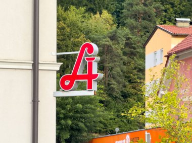 Althofen, Avusturya - 17 Eylül 2025: Kırmızı iş tabelası yeşil ağaçlara karşı duruyor, canlı kentsel çevre ve yerel ticareti vurguluyor