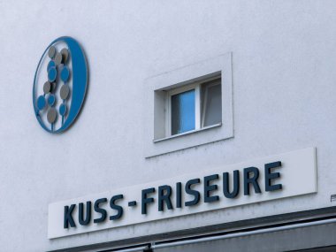 Althofen, Avusturya - 17 Eylül 2025: KUSS-FRISEURE kuaför salonu tabelası, şık bir şehir kuaförünü temsil eden beyaz duvarda modern bir logo barındırıyor