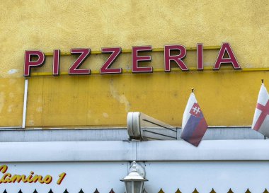 Althofen, Avusturya - 17 Eylül 2025: Pizzacı tabelası parlak sarı bir duvara karşı duruyor, yerel cazibeye bayraklar ekleniyor ve havayı cezbediyor