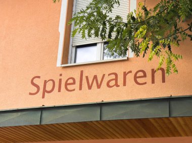 Althofen, Avusturya - 17 Eylül 2025: Şeftali duvarında yeşil yapraklarla çevrili Spielwaren işareti canlı ve davetkar bir şehir manzarası yaratıyor