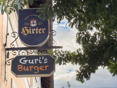 Althofen, Avusturya - 17 Eylül 2025: Guris Burger tabelası ağaç dallarının altına asılarak, bu manzaralı ortamda restoranlar için hoş geldin havası yaratıyor.