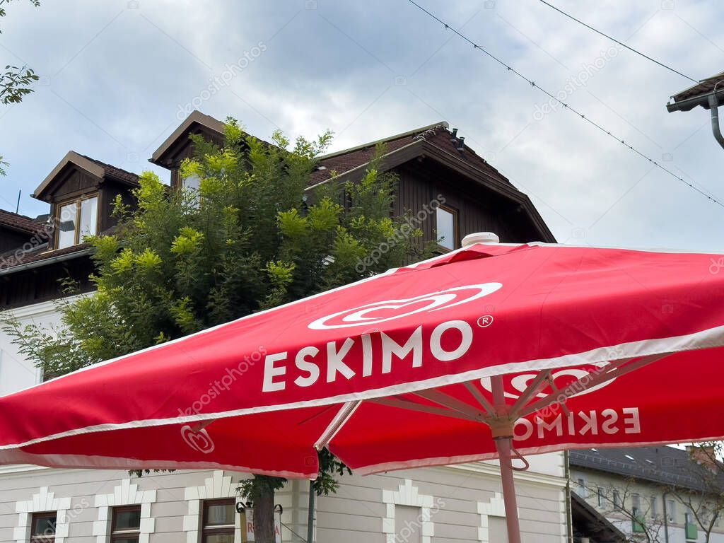 Althofen, Austria - September 17, 2025: Red umbrella with Eskimo branding is set in a charming outdoor area, surrounded by trees and classic buildings