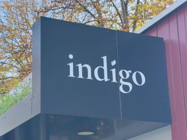 Graz, Avusturya - 11 Ekim 2025: İndigo işareti renkli sonbahar yapraklarına karşı duruyor, alışveriş yapanlar ve yoldan geçenler için hoş bir ortam yaratıyor