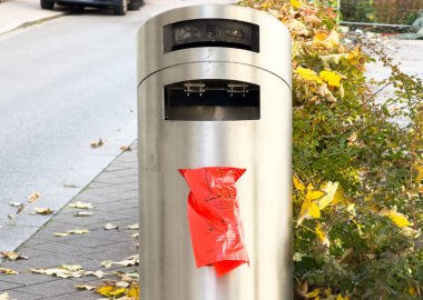 Graz, Avusturya - 11 Ekim 2025: Paslanmaz çelik çöp tenekesinde renkli sonbahar yaprakları ve geçen arabalarla bir şehir caddesinde kırmızı uyarı işareti yer alıyor