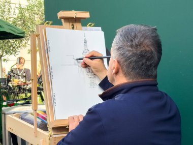 Graz, Avusturya - 11 Ekim 2025: Erkek sanatçı yeşillik ve canlı bir atmosferle çevrili açık havada bir dönüm noktası çizmeye odaklandı