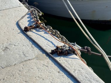 Denizcilik zincirlerinin ve halatın yakın plan çekimleri, arka planda tekneyle taş bir rıhtıma bağlandı..