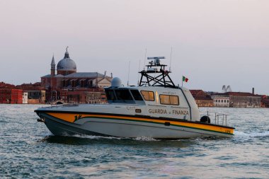 Venedik, İtalya - 23 Haziran 2025: Guardia di Finanza teknesi Venedik sularında tarihi binalar ve günbatımı gökyüzü ile geziyor.