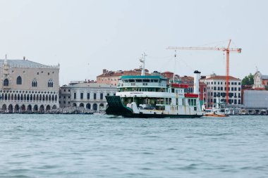 Venedik, İtalya - 23 Haziran 2025: Feribot tarihi binalar ve vinçlerle Venedik sularında seyahat ederek şehir yaşamını resmediyor
