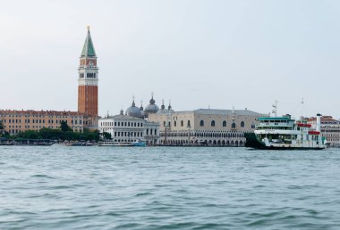 Venedik, İtalya - 23 Haziran 2025: Venedik 'te St. Mark' s Campanile ve Büyük Kanal boyunca sakin sularda süzülen bir tekneyle tarihi binalar sergileniyor
