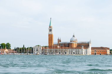 Venedik, İtalya - 23 Haziran 2025: Güzel San Giorgio Maggiore Adası yakınında sakin sular ve tekneler bulunan tarihi bir kilise ve çan kulesi barındırıyor.