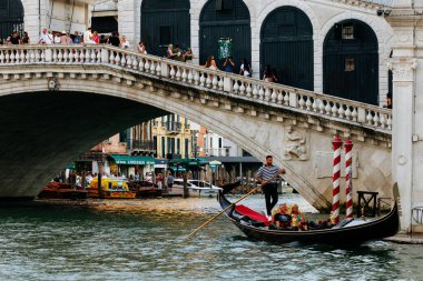 Venedik, İtalya - 23 Haziran 2025: Gondol Venedik 'te Rialto Köprüsü' nün altındaki Büyük Kanal 'da süzülerek canlı atmosfer ve çarpıcı mimariyi yakalıyor.