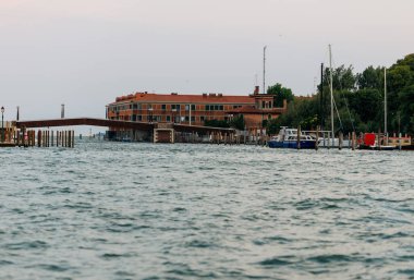 Venedik, İtalya - 23 Haziran 2025: Rıhtımda tekneleri olan, yeşil ve sakin sularla çevrili, huzurlu kıyı yaşam tarzını gösteren liman oteli