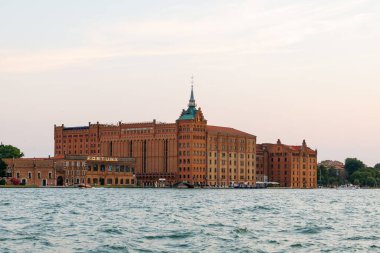 Venedik, İtalya - 23 Haziran 2025: Venedik 'te deniz kenarındaki ikonik kırmızı tuğla yapı, çarpıcı mimari ve sıcak gün batımı renklerini vurguluyor, seyahat görüntüleri için ideal