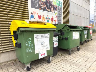 Villach, Avusturya - 23 Ekim 2025: Renkli geri dönüşüm kutuları, atık yönetimi ve geri dönüşüm uygulamalarının önemini vurgulayan dokulu bir duvara karşı yerleştirilmiştir
