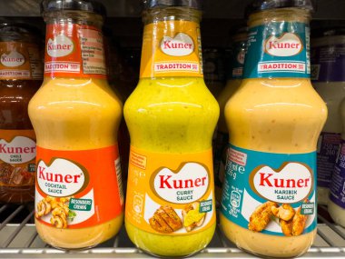 Villach, Avusturya - 23 Ekim 2025: Cam şişelerdeki Kuner sosları süpermarket rafında, yemek meraklıları için kokteyl, köri ve barbekü lezzetleri sergileniyor