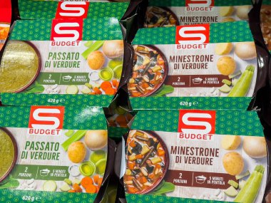 Tarvisio, İtalya - 17 Ekim 2025: S Bütçe sebze çorbası ve sebze püresi paketleri, uygun yemek seçeneklerini ve renkli tasarımları ön plana çıkaran bir markette düzenlenmiştir.