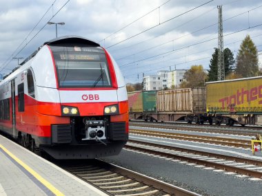 Villach, Avusturya - 29 Ekim 2025: OBB treni bir tren istasyonundaki platforma yaklaşıyor, arka planda yük vagonları görülebiliyor, kentsel ulaşımı vurguluyor