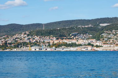 Trieste, İtalya - 14 Ekim 2025: Kıyı kenti açık gökyüzü ile pitoresk bir deniz manzarası yaratan renkli binalar ve yeşil tepeler barındırıyor