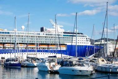 Trieste, İtalya - 14 Ekim 2025: Büyük yolcu gemisi küçük yatları ve yelkenli tekneleriyle marinaya yanaşmış, hareketli bir deniz atmosferi yaratıyor.