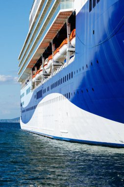 Trieste, İtalya - 14 Ekim 2025: Büyük bir yolcu gemisi, modern deniz tasarımını yansıtan, sakin sulara demirlemiş, görünür cankurtaran botlarıyla çarpıcı mavi ve beyaz bir gövdeye sahiptir.