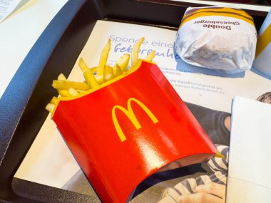 Villach, Avusturya - 10 Kasım 2025: McDonald 's kızarmış patatesleri hamburger ve promosyon ürünleriyle tepside, fast food kültürü ve yemek atmosferini vurguluyor