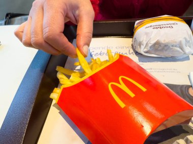 Villach, Avusturya - 10 Kasım 2025: El McDonald 's' ın ikonik kırmızı konteynırından lezzetli patates kızartmaları alıyor, fast food kültürünü ve günlük yemek yemeklerini vurguluyor
