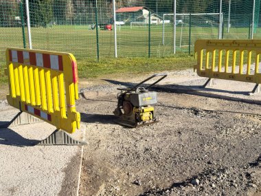 Villach, Avusturya - 10 Kasım 2025: İnşaat alanında sarı bariyerler ve çakıl üzerinde güvenlik ve yol çalışmalarını vurgulayan bir sıkıştırma makinesi yer alıyor