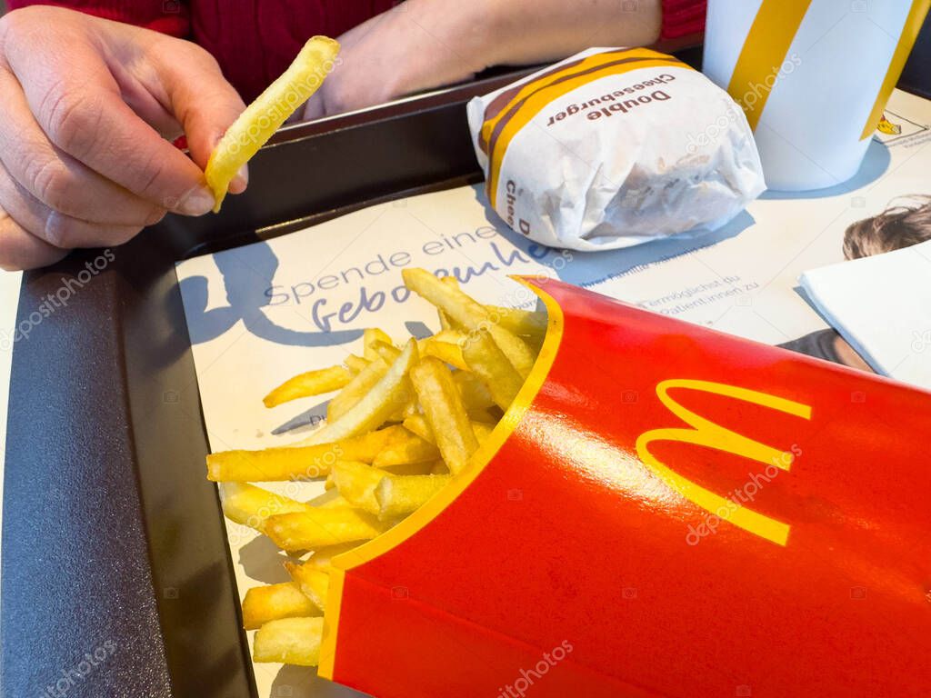Villach, Austria - November 10, 2025: Customer's hand is reaching for a French fry beside a McDonald's burger and drink on a tray with copy space