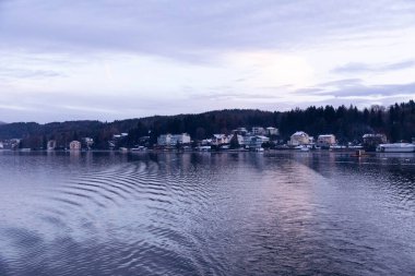 Velden, Avusturya - 20 Aralık 2024: Schlosshotel am Woerthersee huzurlu bir göl, güzel binalar ve neşeli bir Advent ambiyansı ile kış manzarası sergiliyor